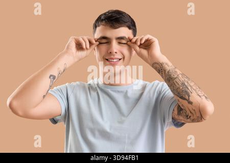 Junger Mann, der Gesichtsaufbauübung auf beigefarbenem Hintergrund macht Stockfoto
