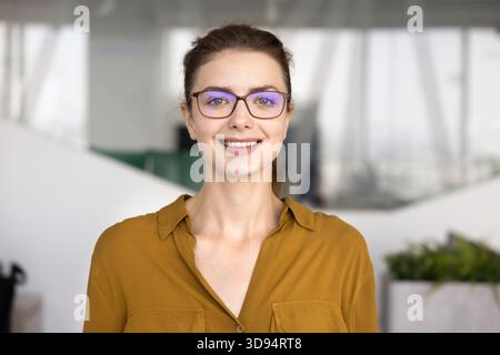 Glückliche junge Geschäftsfrau in stilvoller Brille, die im Büro posiert Stockfoto
