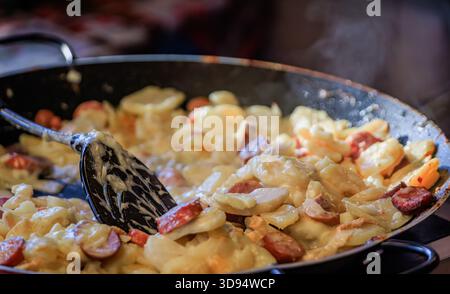 Traditionelle elsässische Tartellette mit Reblochon-Käse, Würstchen und Kartoffeln in einer großen Pfanne auf dem Weihnachtsmarkt in Colmar, Frankreich Stockfoto