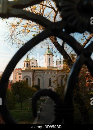 Ein ruhiger Blick auf eine historische Kirche mit grünen Kuppeln, kunstvoll eingerahmt durch kunstvoll verzierte schmiedeeiserne Zäune Stockfoto