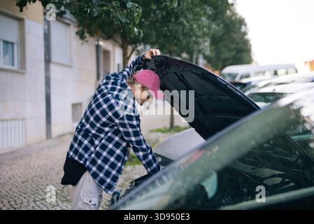 Junger Mann, der tagsüber auf der Wohnstraße einen Automotor diagnostiziert Stockfoto