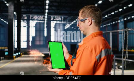 Vertikaler Chroma-Schlüssel mit schwarzem Personal arbeitet in Industrieanlagen mit Schutzausrüstung und unterstützt die logistische Koordination mit Geräten in der Fabrikhalle. Schwermetallbetrieb. Stockfoto