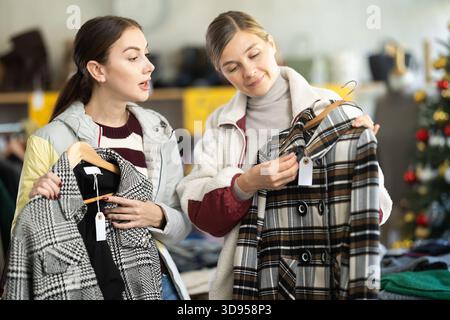 Zwei Frauen, die sich zu Weihnachten in einem Bekleidungsgeschäft einen Mantel oder eine Jacke aussuchen Stockfoto