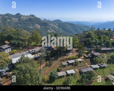 Friedliche Luftaufnahme des abgelegenen ländlichen Dorfes auf dem Berg in Thailand. Malerische Landschaft mit traditioneller Siedlung in der Natur, umgeben von grünen Fo Stockfoto