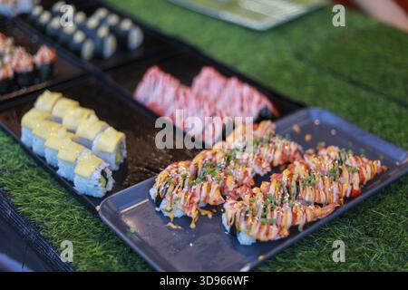 Appetitliche Auswahl an japanischen Sushi-Rollen. Köstliches Maki mit Mayonnaise-Sauce auf schwarzem Tablett, herzhafte Mahlzeit bereit zum Abendessen am Essensstand. Fre Stockfoto