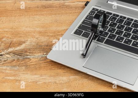 Eine Lupe sitzt auf der Tastatur eines Laptops auf einem rustikalen Holztisch. Die Szene deutet auf Neugier und die Erforschung digitaler Inhalte hin. Stockfoto