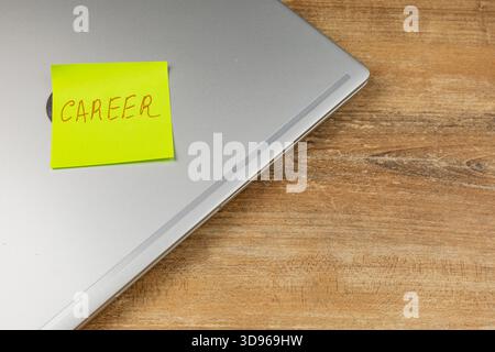 Ein leuchtend gelber Haftnotiz mit der Aufschrift Career befindet sich an der Ecke eines silbernen Laptops auf einem hölzernen Schreibtisch in gemütlicher Atmosphäre im Heimbüro. Stockfoto