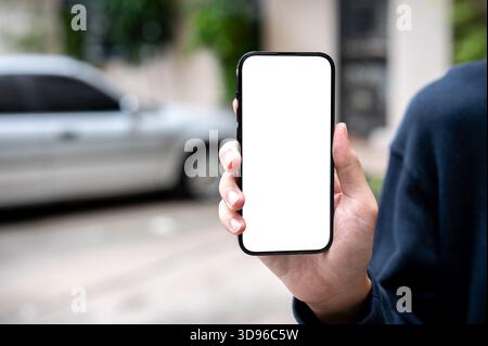 Nahaufnahme der Hand des Mannes, der das Smartphone mit weißem Bildschirm hält, während er auf dem Parkplatz steht. Nachrichten und Updates, Werbemockup, Online-Gesellschaft. Stockfoto
