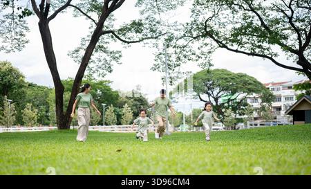 Dad hält eine Leine an Corgi-Welpen, während er mit Mutter Sohn und Tochter auf dem Gras im Park Alongs läuft. Eltern und Kinder, Hund, Familienausflug. Stockfoto