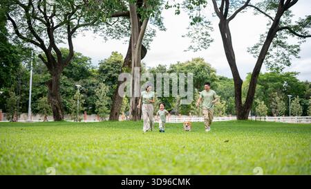 Vater oder Vater halten eine Leine an Corgi-Welpen, während er läuft oder läuft, Mama und Sohn auf Gras im Park. Eltern und Kinder, Hund, Familienausflug. Stockfoto