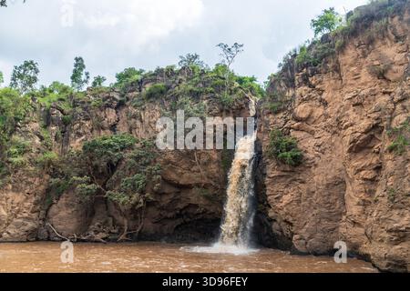 Die Malika Falls im Nakuru National Park, Kenia, sind ein atemberaubender Wasserfall, der sich über felsige Klippen stürzt und von üppigem Grün umgeben ist. Das Wasser fließt in einen kleinen Pool, der Nebel und ein beruhigendes Geräusch erzeugt, während die lebhafte Vegetation um die malerische Schönheit der Szene beiträgt. Stockfoto