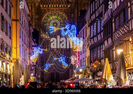 Straßburg, Frankreich - 27. November 2025: Die Menge versammelt sich in einer festlichen Straße mit Weihnachtslichtern und Engelsdekorationen, die nach Straßburg Cathe führt Stockfoto