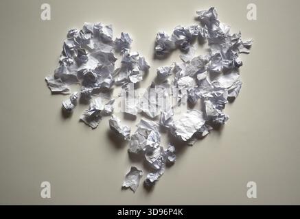 Herzform aus zahlreichen kleinen, zerknitterten weißen Papierstücken, die eine unregelmäßige, gebrochene Textur auf einem neutralen Hintergrund erzeugen. Symbol der Emotionen Stockfoto