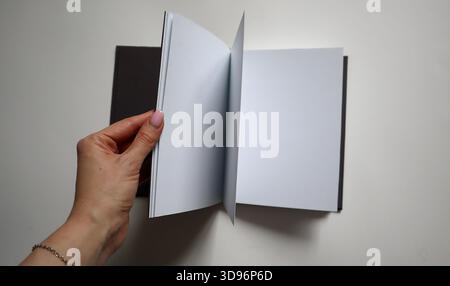 Die Frauenhand hält ein offenes Notizbuch mit leeren weißen Seiten auf hellem Hintergrund. Konzept von Idee, Lernen, Geschäft, ein neues Projekt. Bild ist geeignet Stockfoto