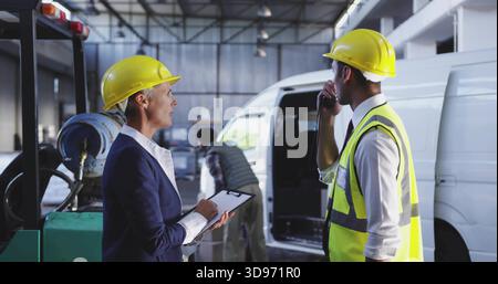 Sprechender Vorgesetzter im Anzug und Vorarbeiter in Warnweste, die Fracht in Garage, Klemmbrett und Radio verladen Stockfoto