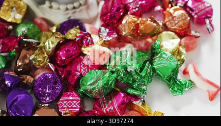 Es werden bunte Bonbons mit Folien- und Twist-Wrap-Verpackung mit gummiartigen Stücken auf weißem Teller gezeigt Stockfoto