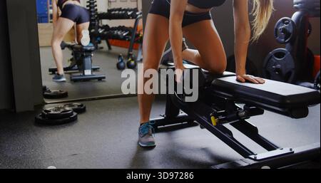 Eine einarmige Reihe auf einer verstellbaren Bank, eine Frau in schwarzer Sportswear, die im Fitnessstudio die Hantel packt Stockfoto