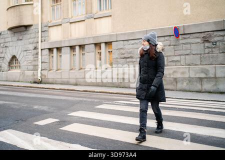 Im Winter überqueren Fußgänger die Straße. Frau in der Stadt auf dem Fußgängerweg, Zebraüberquerung. Mantel oder Jacke. Stockfoto