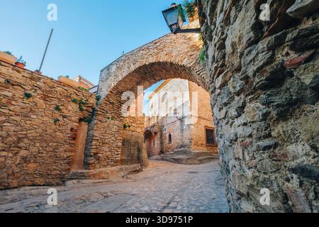 Blick durch einen alten Steinbogen in eine enge, kopfsteingepflasterte Straße im mittelalterlichen Dorf Peratallada, Katalonien, Spanien Stockfoto
