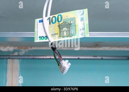 Elektroinstallation für die Renovierung der Beleuchtung, 100 Euro Papierschein hängt an Drähten in einer alten Wohnung, Renovierung der Beleuchtung von Wohnwohnungen mit Stockfoto