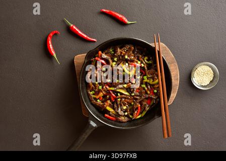 Chinesische Pfanne mit frittiertem, dünn in Streifen geschnittenem Rindfleisch und Paprika auf dunkelbraunem Hintergrund. Draufsicht, flach Stockfoto