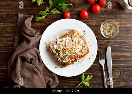 Lasagne mit Hackfleisch, Ricotta und Tomatensauce auf weißem Teller auf hölzernem Hintergrund. Draufsicht, flach Stockfoto