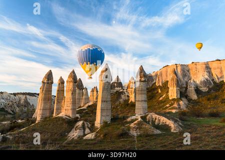 Blick auf Heißluftballons, die sanft über die Feenkamine gleiten und sanfte Schatten auf die raue Landschaft werfen, im Love Valley, Kappadokien, Türkei. Stockfoto