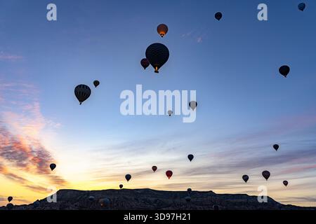 Blick auf Heißluftballons, die gegen den pastellfarbenen Morgenhimmel schweben und eine traumhafte Landschaft im Love Valley, Kappadokien, Türkei schaffen. Stockfoto