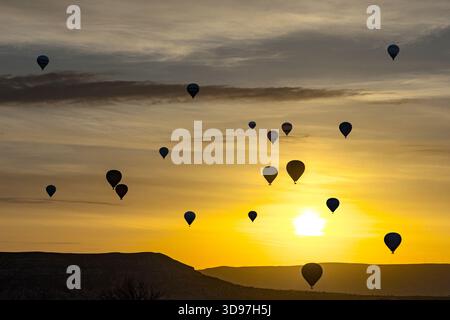 Aus der Vogelperspektive von Heißluftballons, die vor dem pulsierenden, goldenen Sonnenaufgang geschildert sind und den Himmel mit Orange- und Gelbtönen bemalen, Goreme, Kappadokien, Stockfoto