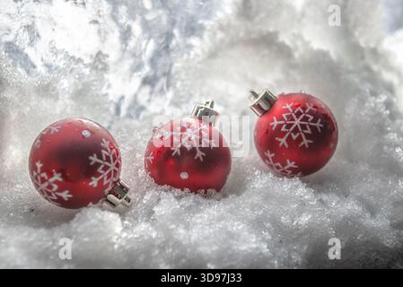 Großaufnahme auf drei roten Weihnachtskugeln mit Schneeflocke auf dem Schnee für Winterkomposition. Stockfoto