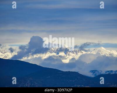Schneebedeckte Bergkette hinter Dark Blue Hills unter einem weichen bewölkten Himmel in Südfrankreich Stockfoto