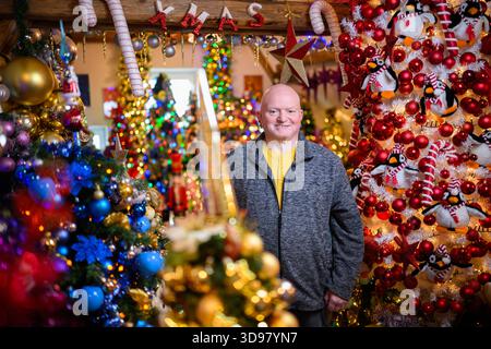 Rinteln, Deutschland. Dezember 2025. Thomas Jeromin steht zwischen den Weihnachtsbäumen in seinem Haus im Stadtteil Schaumburg. 621 Weihnachtsbäume mit weit über 125.000 Weihnachtskugeln und 50.000 Lichtern: Das Haus der Familie Jeromin erstrahlt in der Adventszeit wie eine farbenfrohe Weihnachtswelt. Das Rekordinstitut für Deutschland hat die Familie „für die am meisten dekorierten Weihnachtsbäume an einem Ort“ ausgezeichnet. Quelle: Julian Stratenschulte/dpa/Alamy Live News Stockfoto