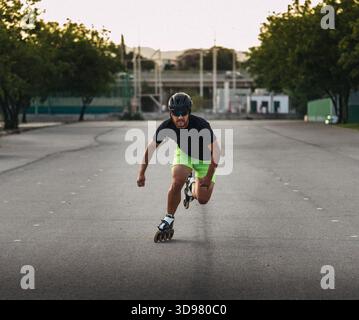 Mann, der sich auf Inlineskaten konzentriert, Schutzhelm und Sonnenbrille auf Asphaltstraßen trägt Stockfoto