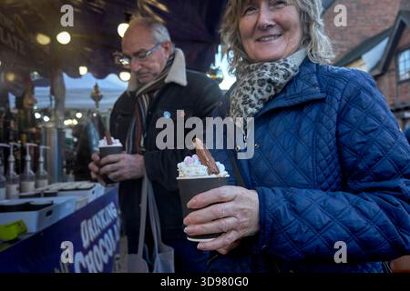 Die Leute genießen ein winterwärmeres Getränk aus heißer Schokolade und Baileys Irish Cream, garniert mit einer Cadburys-Flocke, serviert auf einem Weihnachtsmarkt. England Stockfoto