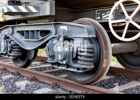 Das Drehgestell aus Metall-Güterwagen mit schweren Stahlfedern und abgenutzter Radoberfläche steht bei Tageslicht auf rostigen Gleisen. Die Industriestruktur zeigt die Federung Stockfoto