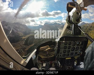 Blick aus dem Inneren des Hubschraubercockpits, das im Herbst bei Tageslicht über Kiefernwald und gewundenen Fluss in Kanada fliegt Stockfoto