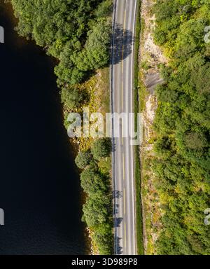 Drohnenansicht der E10-Straße entlang eines dunklen Sees, umgeben von grünem Wald. Lofoten-Inseln Norwegen Stockfoto