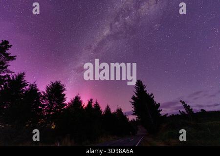 Wunderschöne Milchstraße und Aurora australis über dem Wald auf der Straße in ländlicher Szene auf der Südinsel Neuseelands Stockfoto