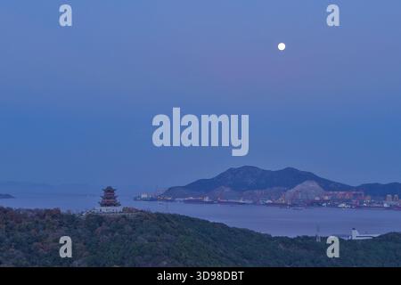 Peking, Chinas Provinz Zhejiang. Dezember 2025. Ein Vollmond ist über einem Hafen im Daishan County, Stadt Zhoushan, ostchinesische Provinz Zhejiang, 4. Dezember 2025 zu sehen. Der zweitgrößte Vollmond in diesem Jahr für die Augen von Mondbeobachtern wird am Freitagmorgen erscheinen, aber die beste Aussichtszeit fällt am Donnerstagabend. Quelle: Xing Shoumiao/Xinhua/Alamy Live News Stockfoto
