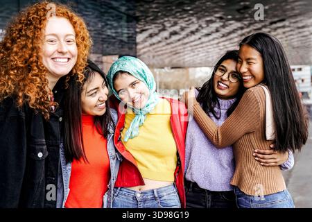 Vielfältige Gruppe junger Frauen, die draußen lächeln und umarmen – Freundschaft, Inklusivität und multikulturelles Konzept Stockfoto