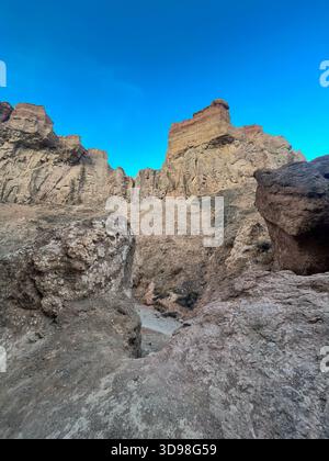 Flacher Blick auf die Felsformationen des Charyn Canyon: Zerklüftete Steinstruktur und burgenähnliche Gipfel vor blauem Himmel. Stockfoto