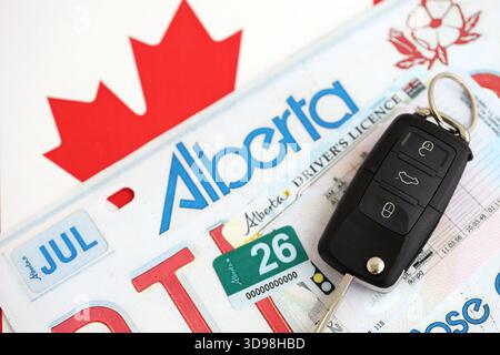 Alberta canadian Autokennzeichen und Zündschlüssel auf der Flagge von Kanada Nahaufnahme. Führerschein- und Zulassungskonzept Stockfoto