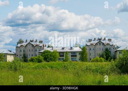 Wohnviertel von Ostrov, Oblast Pskow, Russland, Wohnblöcke hinter einer wilden grünen Wiese an einem Sommertag. Stockfoto
