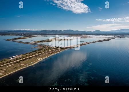 Ein Blick aus der Vogelperspektive auf eine Küstenlandschaft mit geometrischen Salzteichen, engen Straßen, Sardinien, Italien Stockfoto