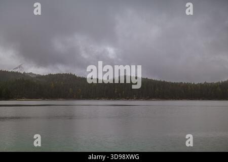 Ein ruhiger See erstreckt sich unter schweren grauen Wolken, umgeben von dunklen bewaldeten Hügeln. Stockfoto