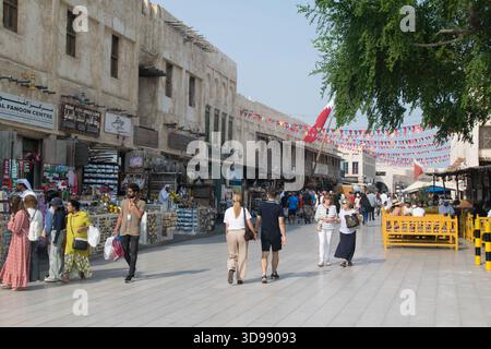 Besucher schlendern durch den lebendigen Souq Waqif in Doha und genießen Geschäfte, Imbissstände und lokales Kunsthandwerk unter einem klaren blauen Himmel. Stockfoto