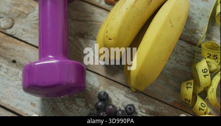Mit lila Hantel mit Reifen Bananen auf Holzplanke, gelbem Klebeband und Heidelbeeren Stockfoto