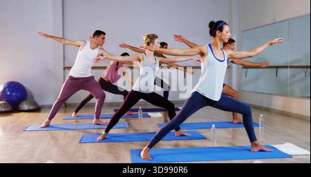 Führender Frontlehrer im weißen Tank, blaue Leggings, die den Kurs auf blauen Matten im Yoga-Studio führt Stockfoto