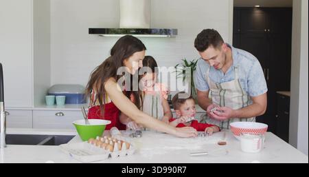 Backenfamilie von vier Personen, die Teig auf der Kücheninsel zubereiten, mit Ausstechern und Schürzen Stockfoto