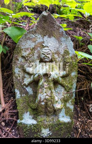 Eine moosbedeckte Myo-o-Statue aus Stein steht versteckt im Wald entlang des historischen Nakasendo-Weges zwischen Magome und Tsumago, Japan Stockfoto